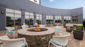 An outdoor patio with a stone fire pit surrounded by wicker chairs and sofas. - Hilton Garden Inn Memphis/Wolfchase Galleria (Cordova)