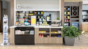 A modern retail kiosk named 'The Shop' with a variety of products including beverages, snacks, and household items. - Hilton Garden Inn Memphis/Wolfchase Galleria (Cordova)