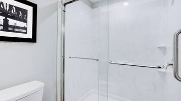 A bathroom with a glass shower enclosure, a white toilet, and a framed picture on the wall.