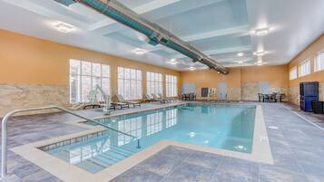 Una gran piscina interior con agua cristalina, rodeada de sillas de descanso y un muro de piedra.