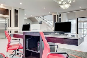 A modern office space with a large desk, two monitors, a red chair, and a staircase in the background. - Holiday Inn & Suites Lafayette North by IHG (Lafayette)