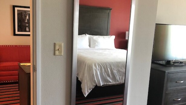 A hotel room with a bed, a large mirror, a red sofa, and a television on a dresser. - Holiday Inn & Suites Lafayette North by IHG (Lafayette)