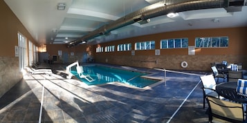 Una piscina con interior iluminado por el sol, zona accesible para sillas de ruedas y área de descanso con mesas y sillas.