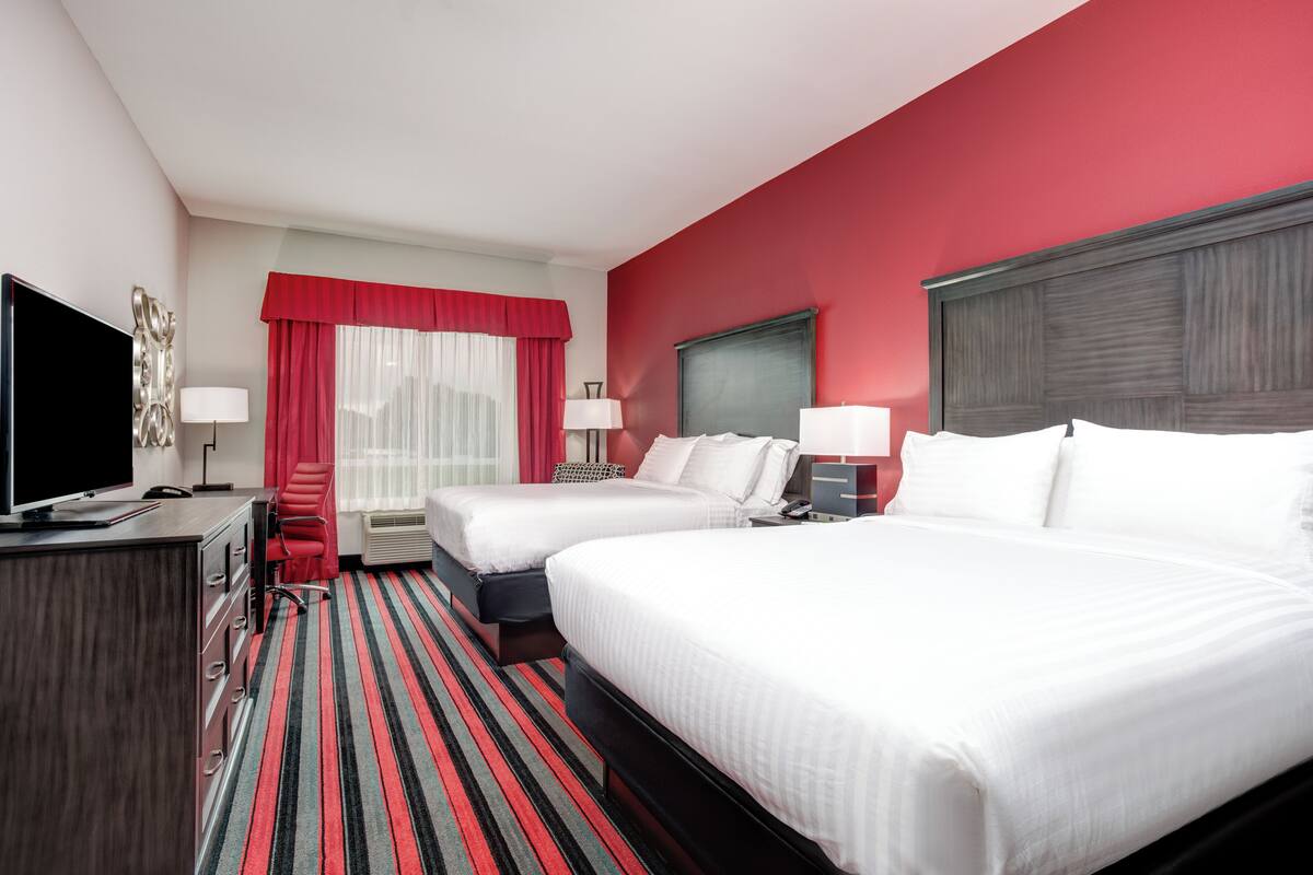 A hotel room with two beds, a TV, a desk, and a red and white color scheme.
