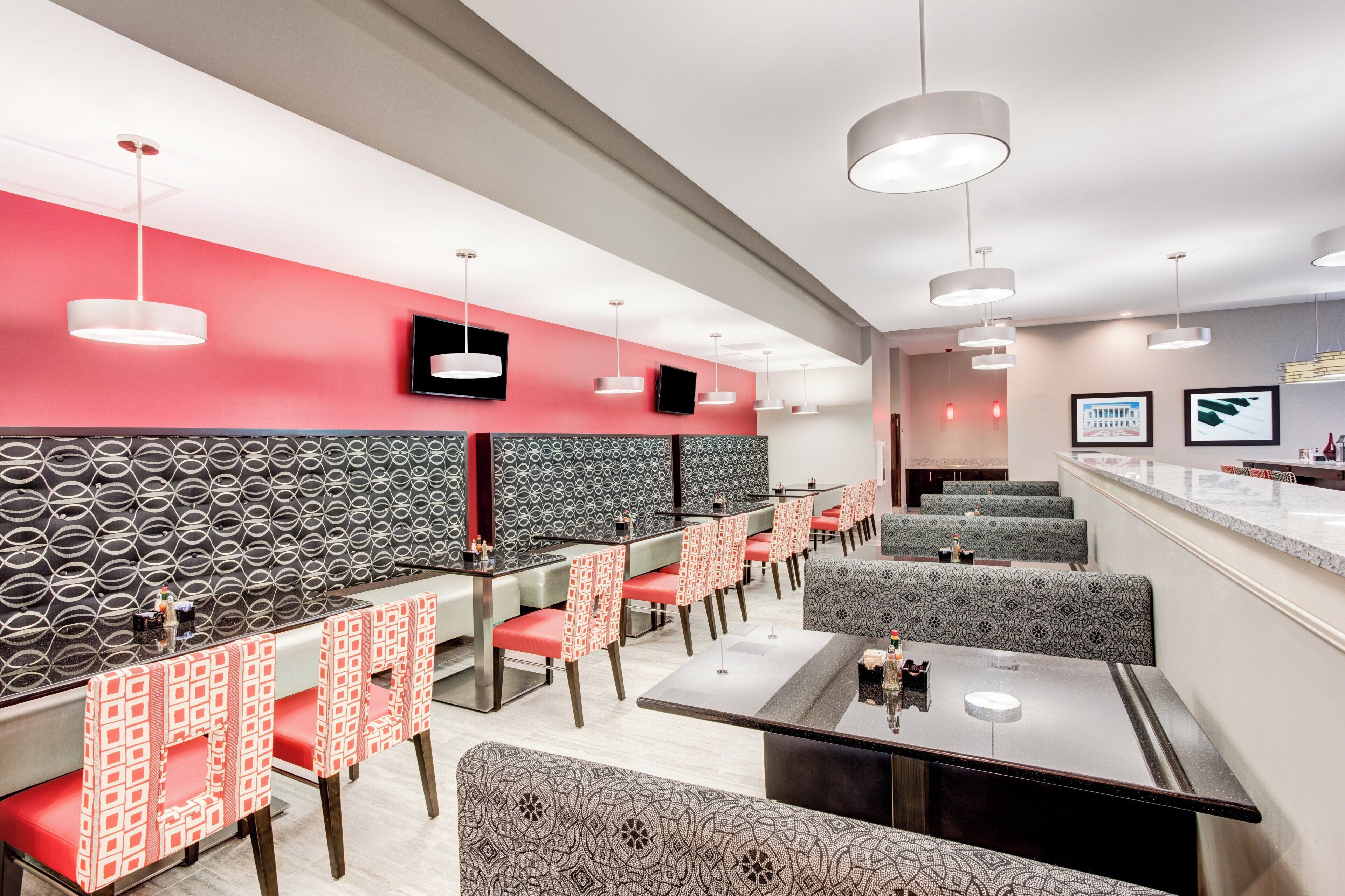 En modern restauranginteriör med rött och grått mönstrade väggar, flera sittgrupper och moderna belysningsarmaturer.