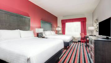 A hotel room with two beds, a desk with a TV, a chair, and a window with red curtains.