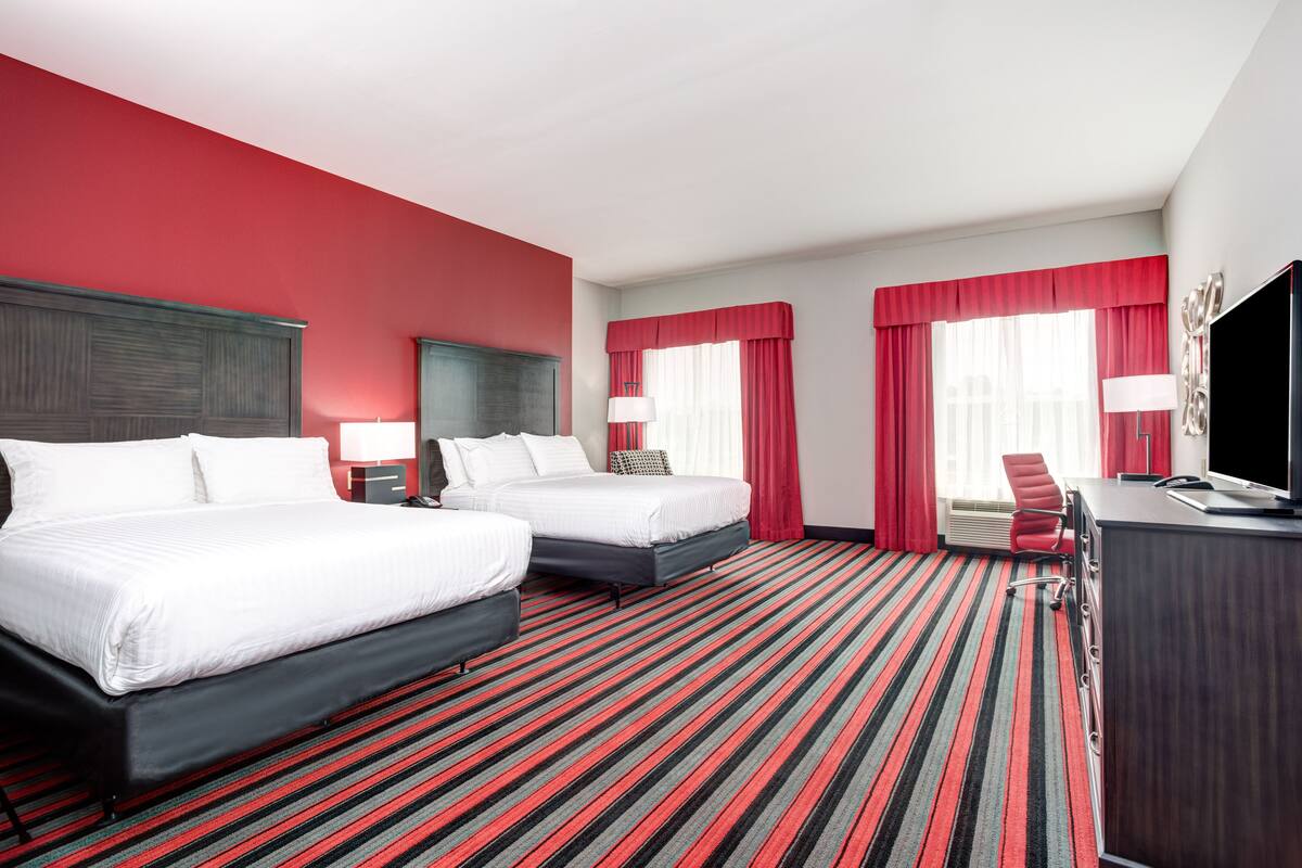 A hotel room with two beds, a desk, a TV, and a red-striped carpet.