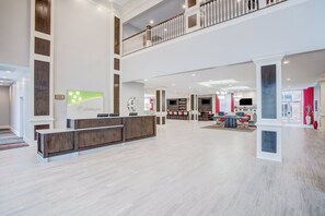 Un hall espacioso con mostrador de recepción, zona de estar y una escalera que sube a un nivel superior.