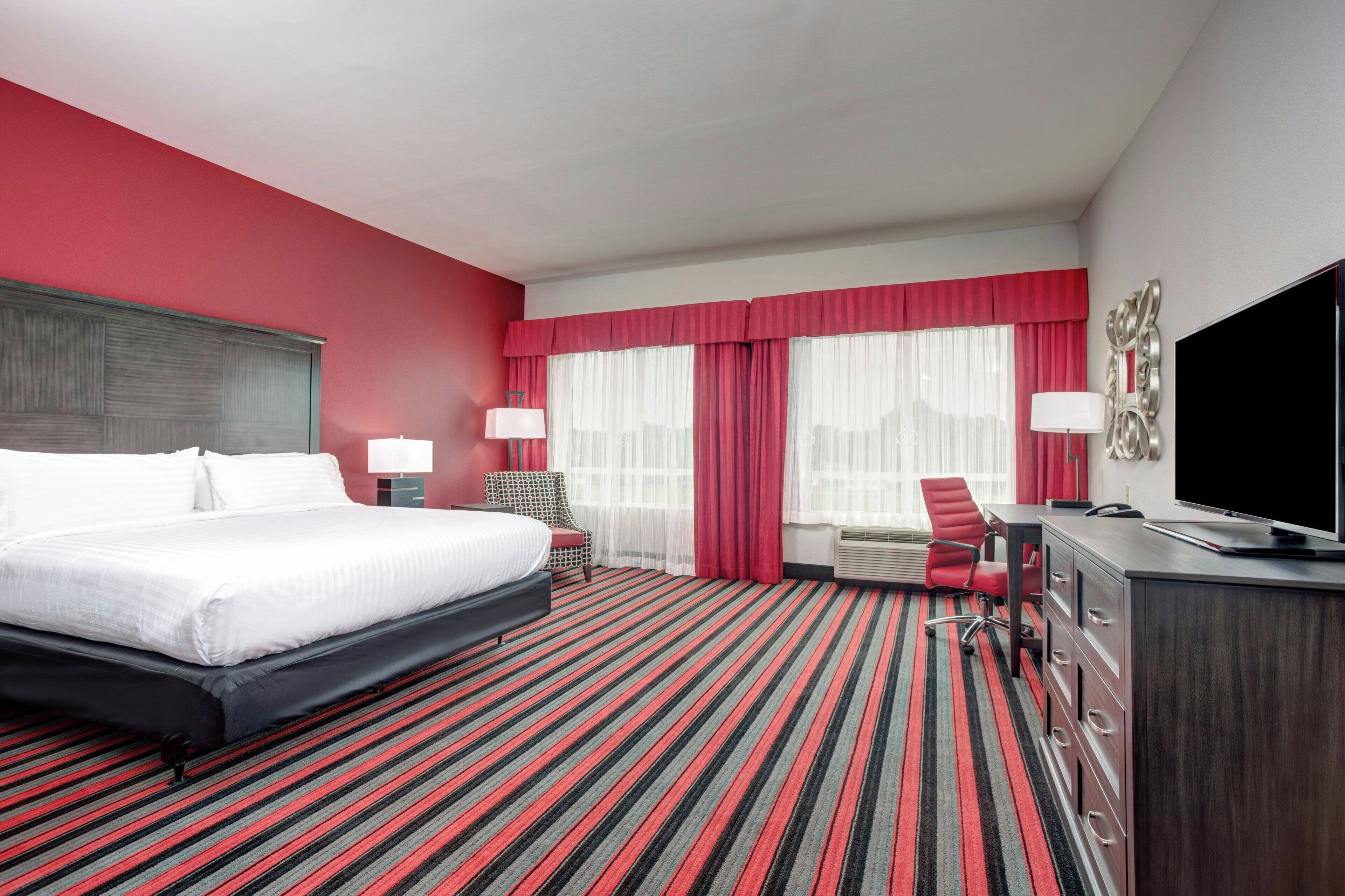 Une chambre d’hôtel avec un grand lit, un bureau, une chaise, une télévision et une fenêtre avec des rideaux.