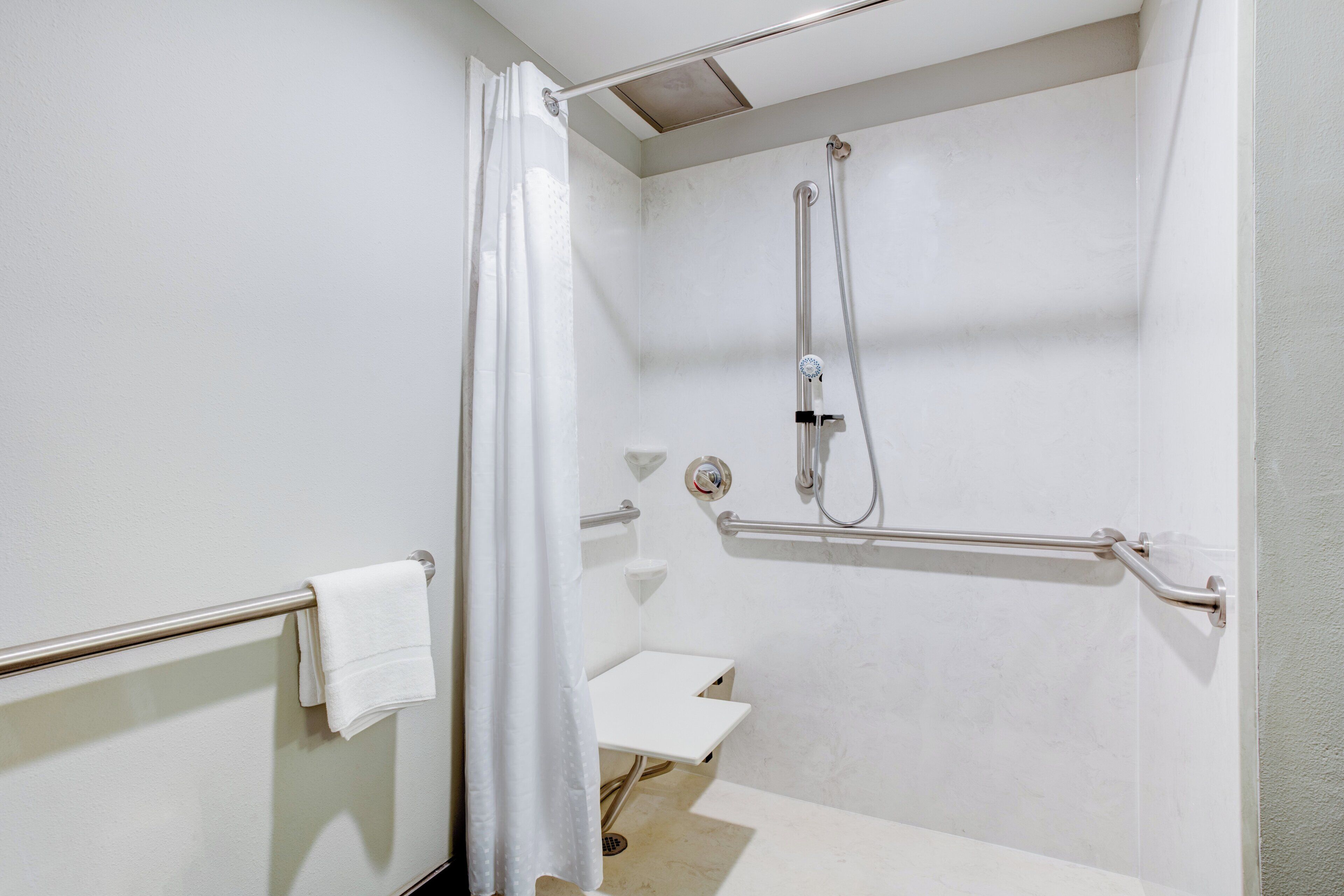 Un baño con ducha, barras de apoyo, inodoro y toallero.