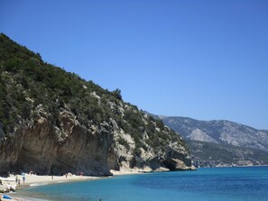 Une plage aux eaux d’un bleu limpide, bordée de falaises rocheuses et dominée par un paysage montagneux.
