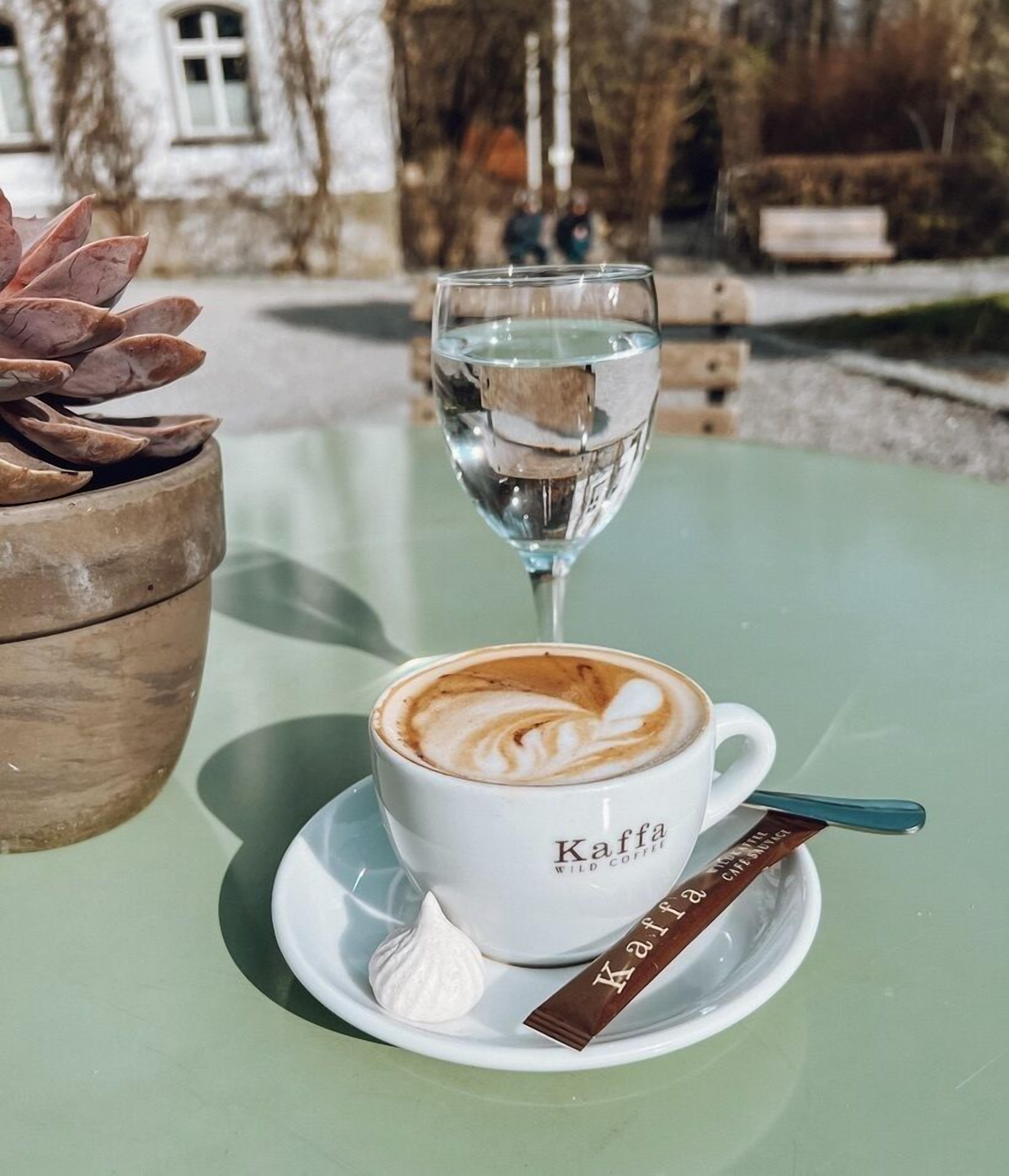 A cup of coffee with latte art labeled "Kaffa Wild Coffee" on a green table.