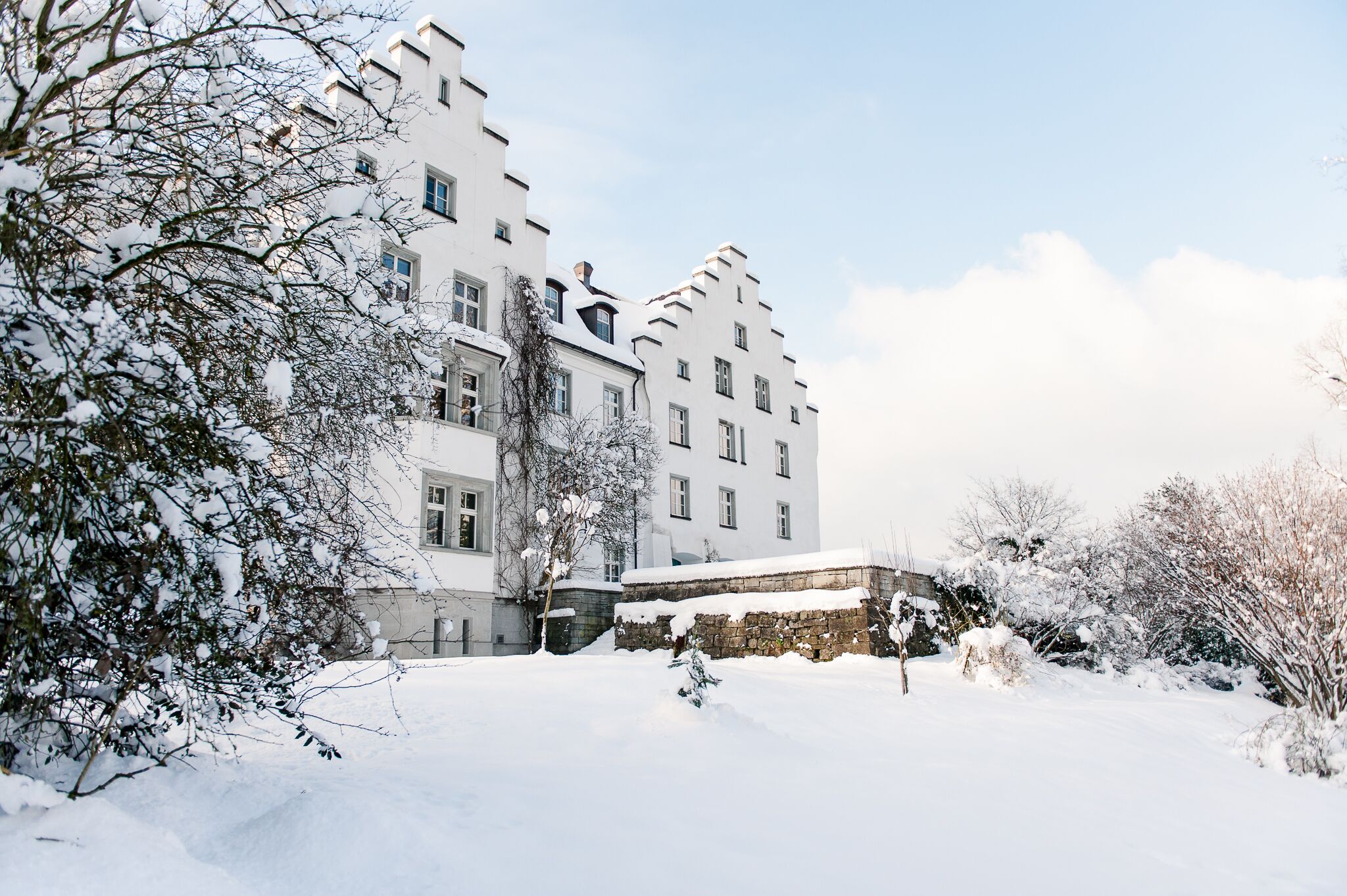 A snow-covered building with multiple windows and a stone wall in the foreground.
