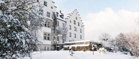 A snow-covered building with multiple windows and a stone wall in the foreground.