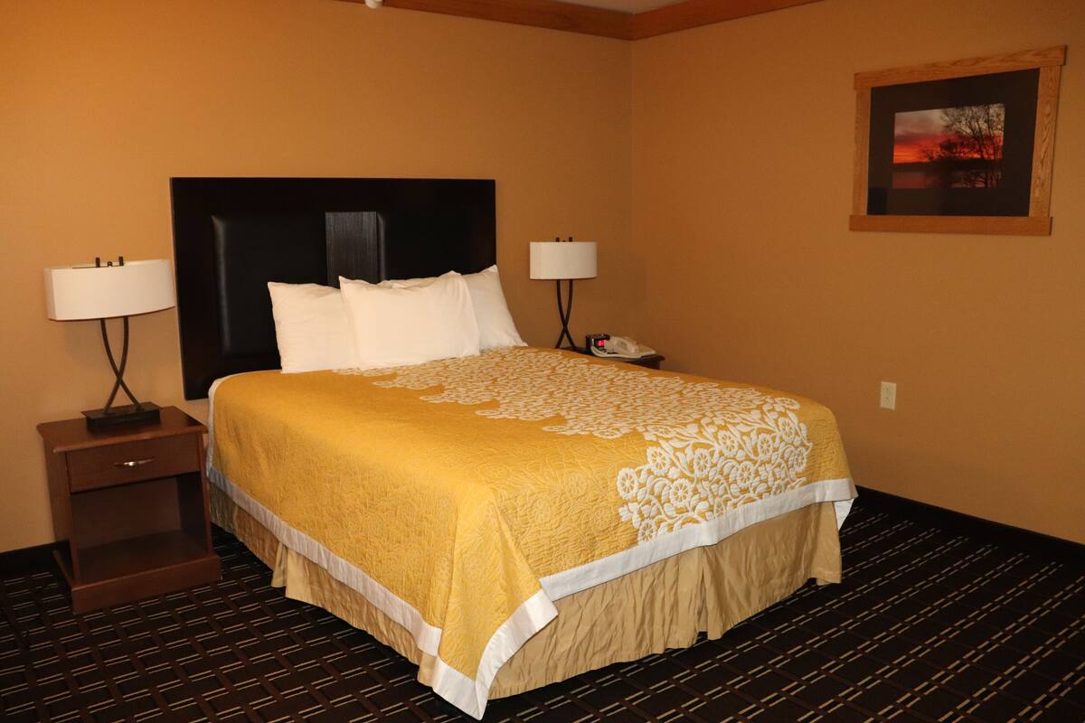 A hotel room with a large bed, two bedside tables with lamps, a nightstand, and a framed picture on the wall.