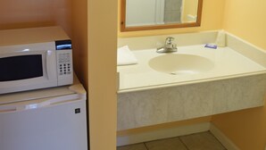 A compact bathroom with a white sink, a mirror, a microwave, and a small refrigerator. - Fort Eustis Inn (Newport News)