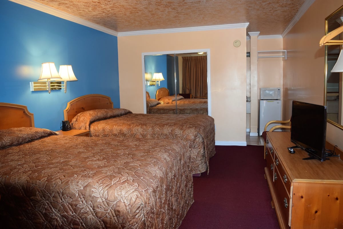 A hotel room with two beds, a television, a dresser, and a microwave.