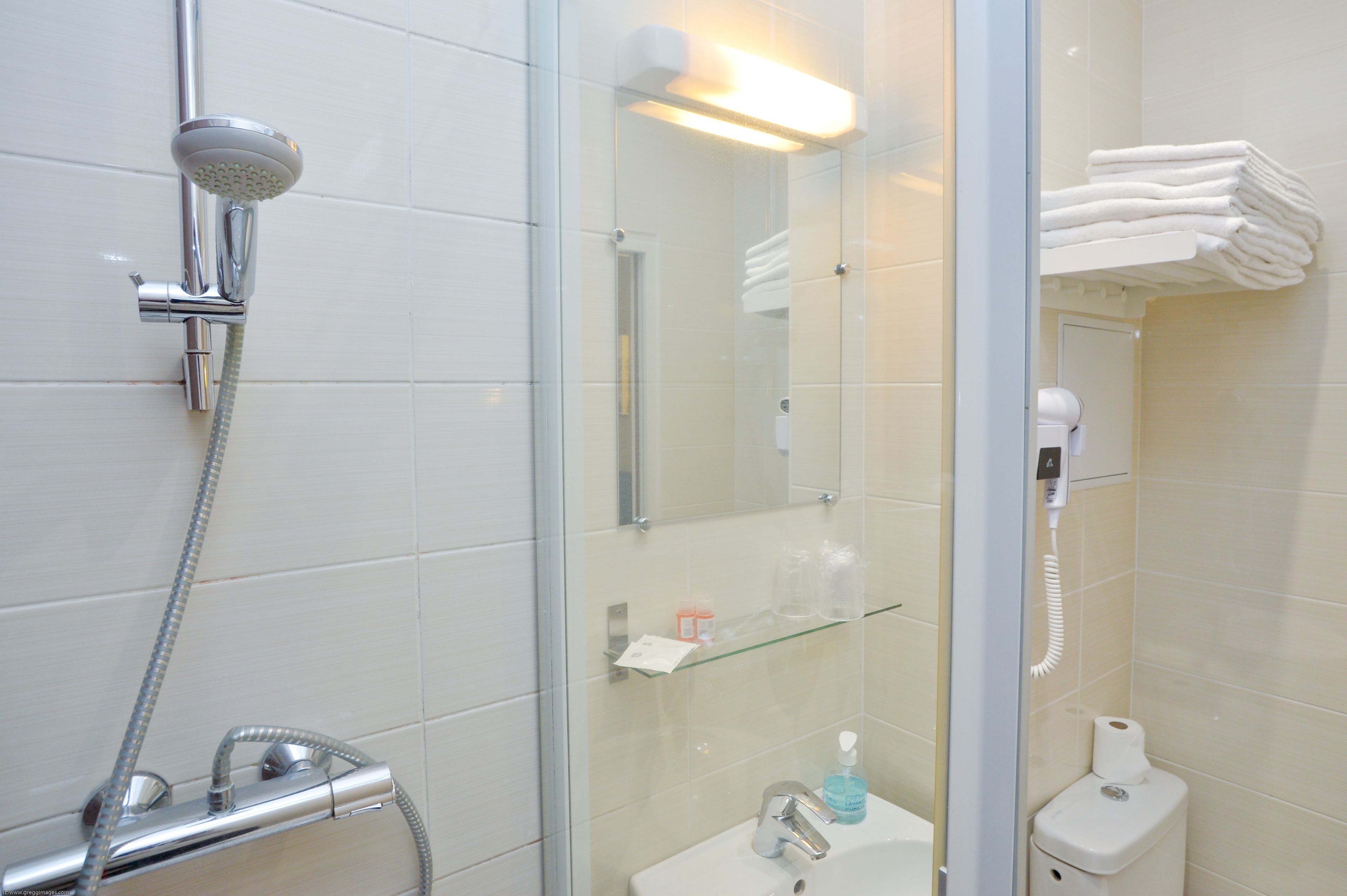 Une salle de bain équipée d’une douche, d’un lavabo et de toilettes, ainsi que d’une étagère en verre où sont rangés les articles de toilette.