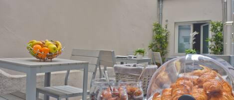 A table with a fruit bowl, jars of nuts, and a covered display of pastries.