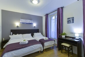 A hotel room with two beds, a desk, a chair, a window with curtains, a wall-mounted lamp, a small plant, and a painting. - Hotel du Quai de Seine (Paris)