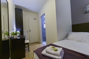 A hotel room with a bed, a desk with a plant, a chair, and a door leading to a balcony. - Hotel du Quai de Seine (Paris)