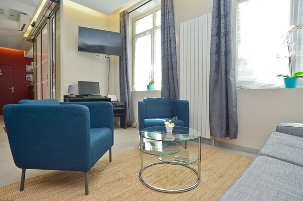 A modern living room with blue armchairs, a glass coffee table, and a grey sofa. - Hotel du Quai de Seine (Paris)