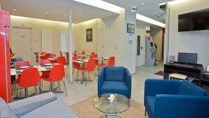 Un moderno vestíbulo de hotel con asientos rojos y azules, una mesa de vidrio y un televisor sobre un escritorio.