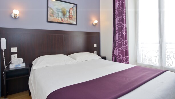 Habitación de hotel con cama, mesita de noche con teléfono y pañuelos, un cuadro en la pared y una ventana con cortinas.