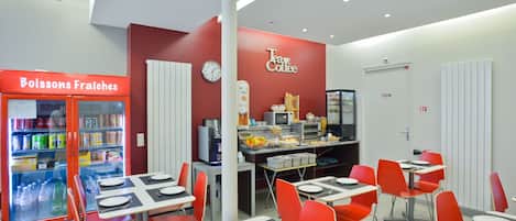 A cafeteria with red chairs, tables set for dining, a coffee station, and a refrigerator with beverages.