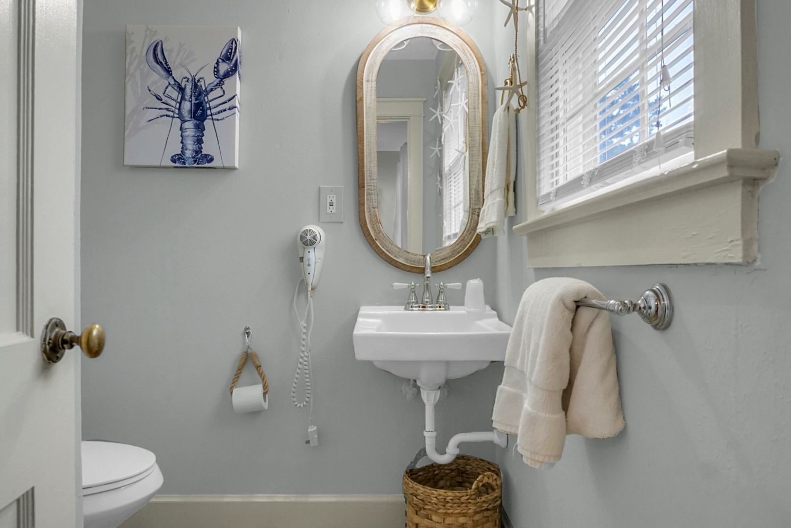 A bathroom with a white sink, a mirror, a towel rack, a toilet, and a decorative lobster painting.