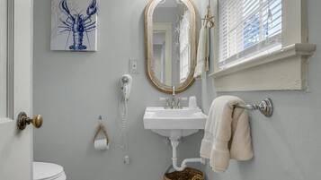 A bathroom with a white sink, a mirror, a towel rack, a toilet, and a decorative lobster painting.