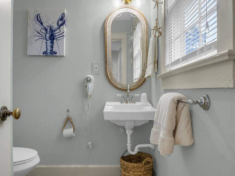 A bathroom with a white sink, a mirror, a towel rack, a toilet, and a decorative lobster painting.