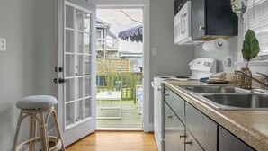 A kitchen with a view to a backyard, a white refrigerator, a microwave, a sink, and a wooden stool. - Carolina Beach Inn (Carolina Beach)