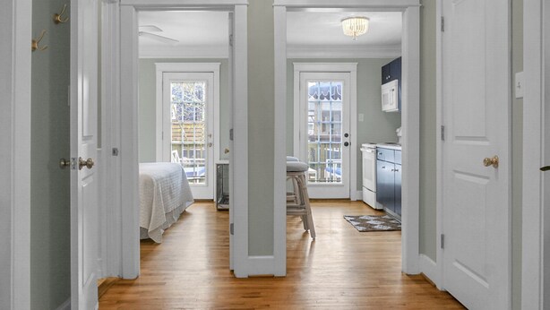 A narrow hallway with wooden flooring, white walls, and doors leading to a bedroom and a kitchen area. - Carolina Beach Inn (Carolina Beach)