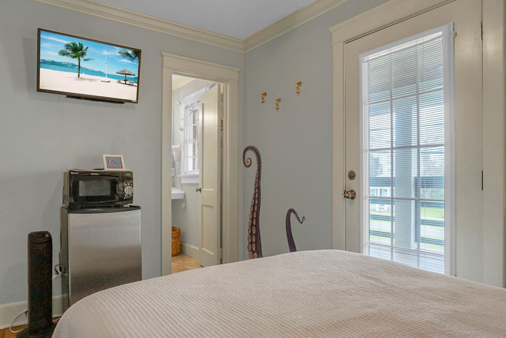 A bedroom with a bed, a television on the wall, a microwave, and a door with a decorative handle.