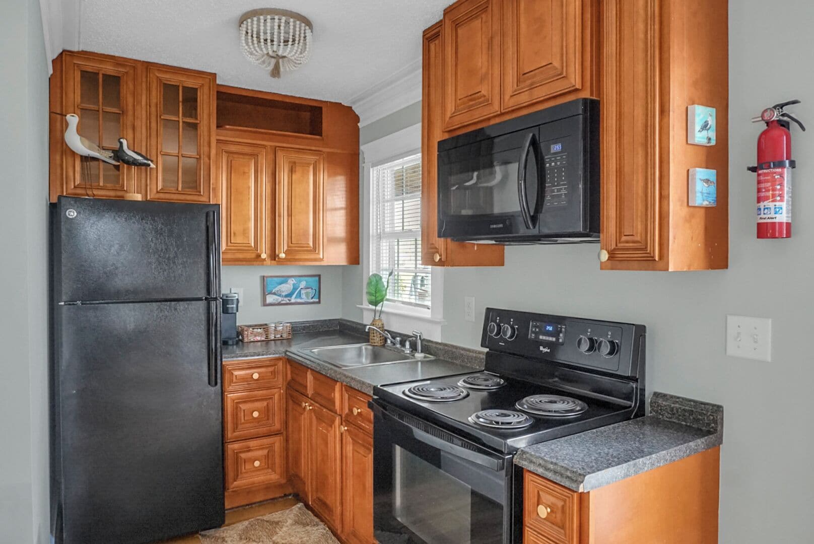 A kitchen with wooden cabinets, a black refrigerator, a microwave, a stove, and a sink.