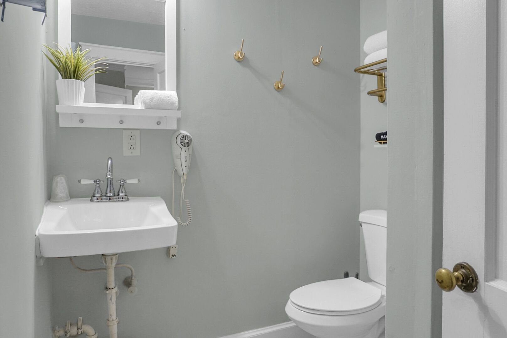 Un baño con lavamanos blanco, secador de pelo, inodoro y espejo.