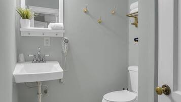 Un baño con lavamanos blanco, secador de pelo, inodoro y espejo.