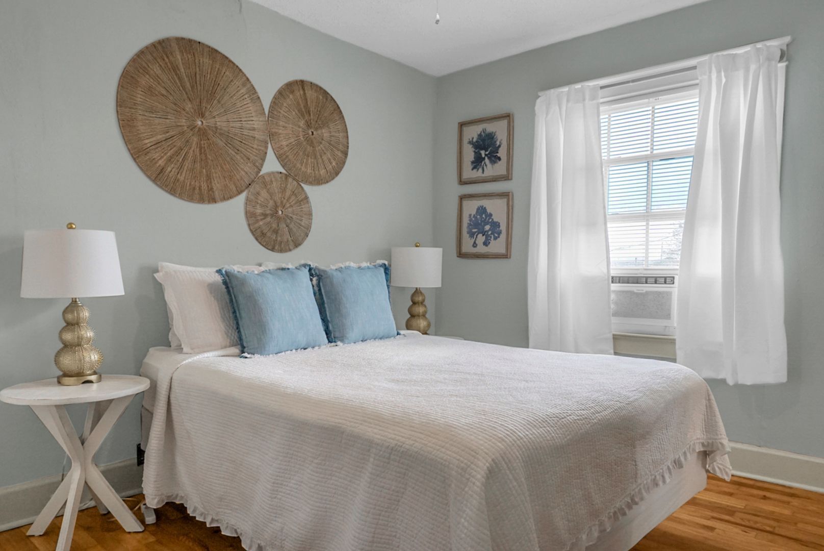 Un dormitorio con una cama grande, dos mesitas de noche con lámparas, una ventana con cortinas blancas y decoración en la pared.