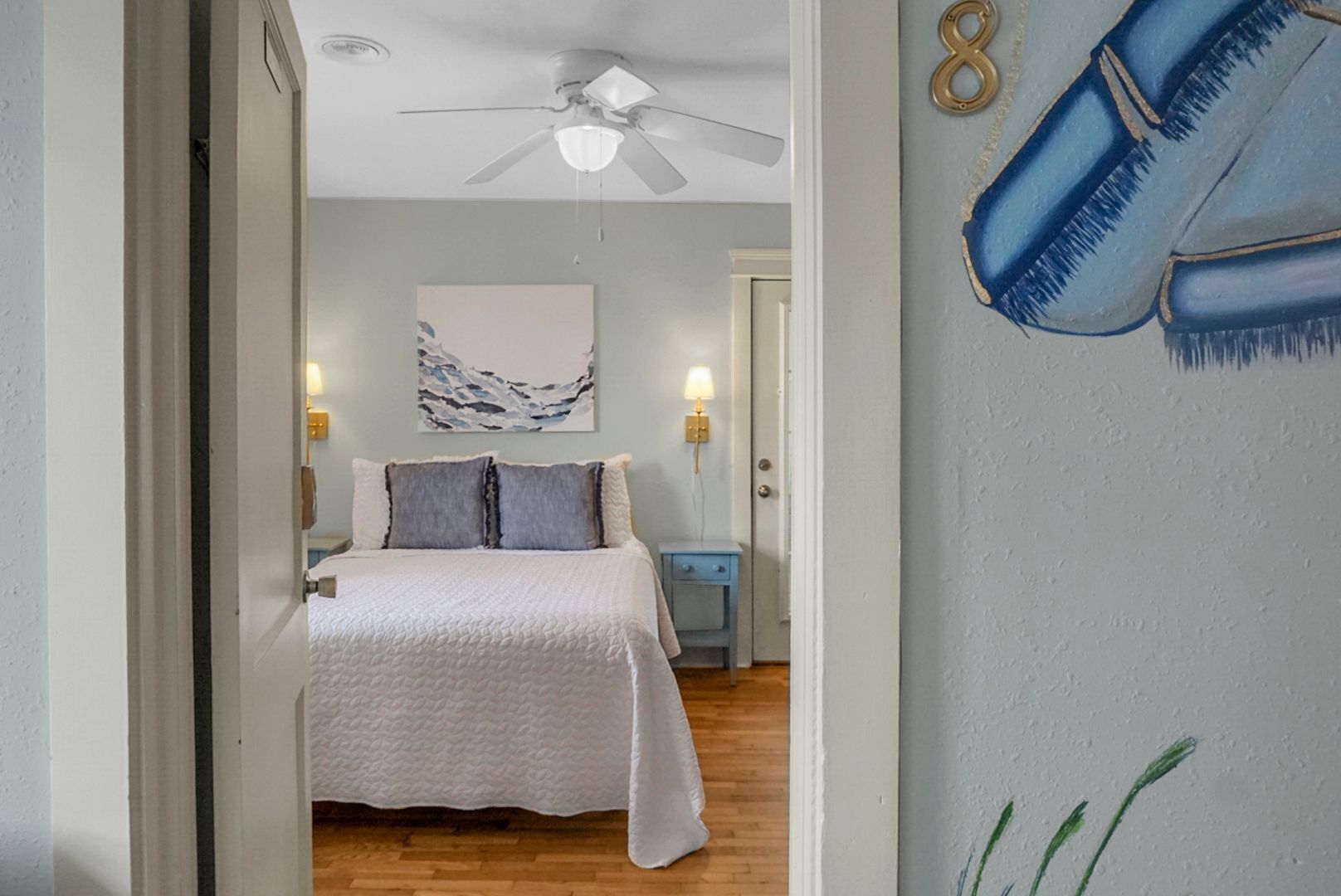 A bedroom with a bed, a ceiling fan, a nightstand, and a wall with a number eight mural.
