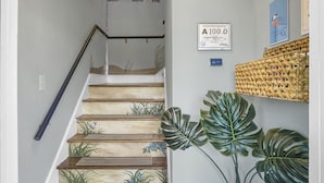 A staircase with wooden steps and a handrail, a wall-mounted sanitation rating sign, and a woven basket decoration. - Carolina Beach Inn (Carolina Beach)