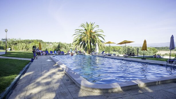 A swimming pool with lounge chairs and umbrellas, surrounded by greenery and a clear sky. - Hotel Urgeiriça (Nelas)
