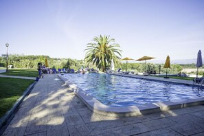 A swimming pool with lounge chairs and umbrellas, surrounded by greenery and a clear sky. - Hotel Urgeiriça (Nelas)