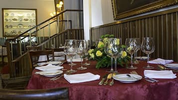 Mesa de jantar posta com toalhas brancas, copos de vinho e talheres, rodeada por cadeiras em restaurante com decoração em madeira e escadaria.