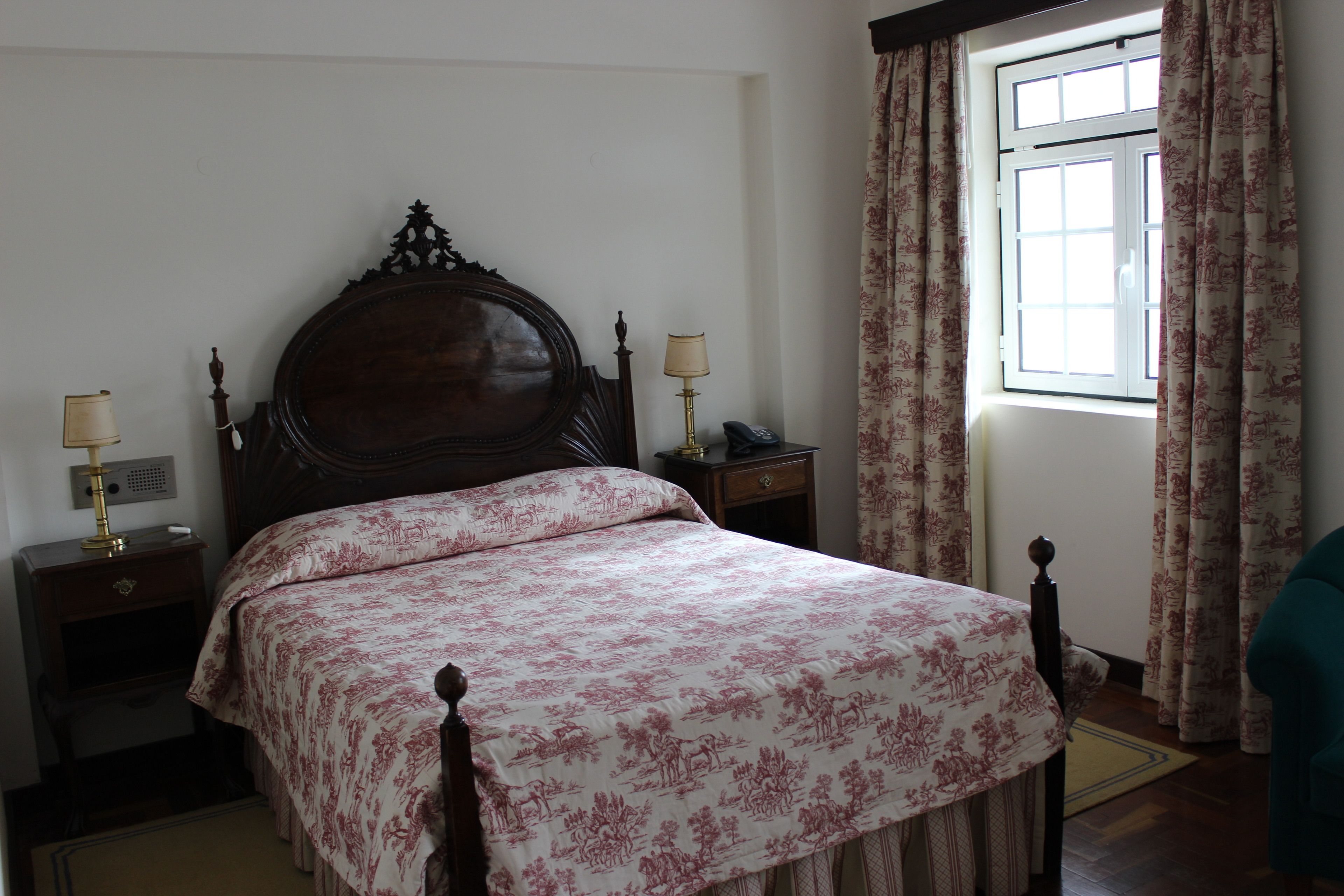 Un dormitorio con una cama grande, dos mesitas de noche con lámparas, una ventana con cortinas y una silla.