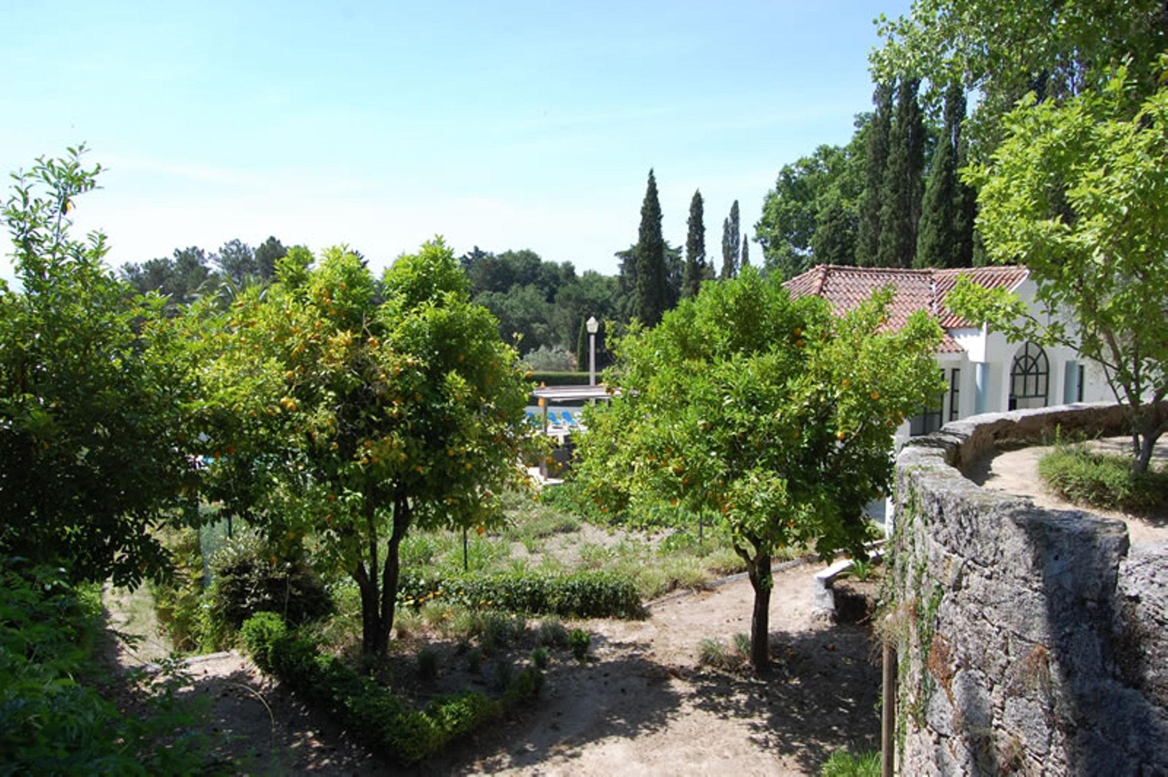 A historic building with a stone wall and a garden with trees and shrubs.