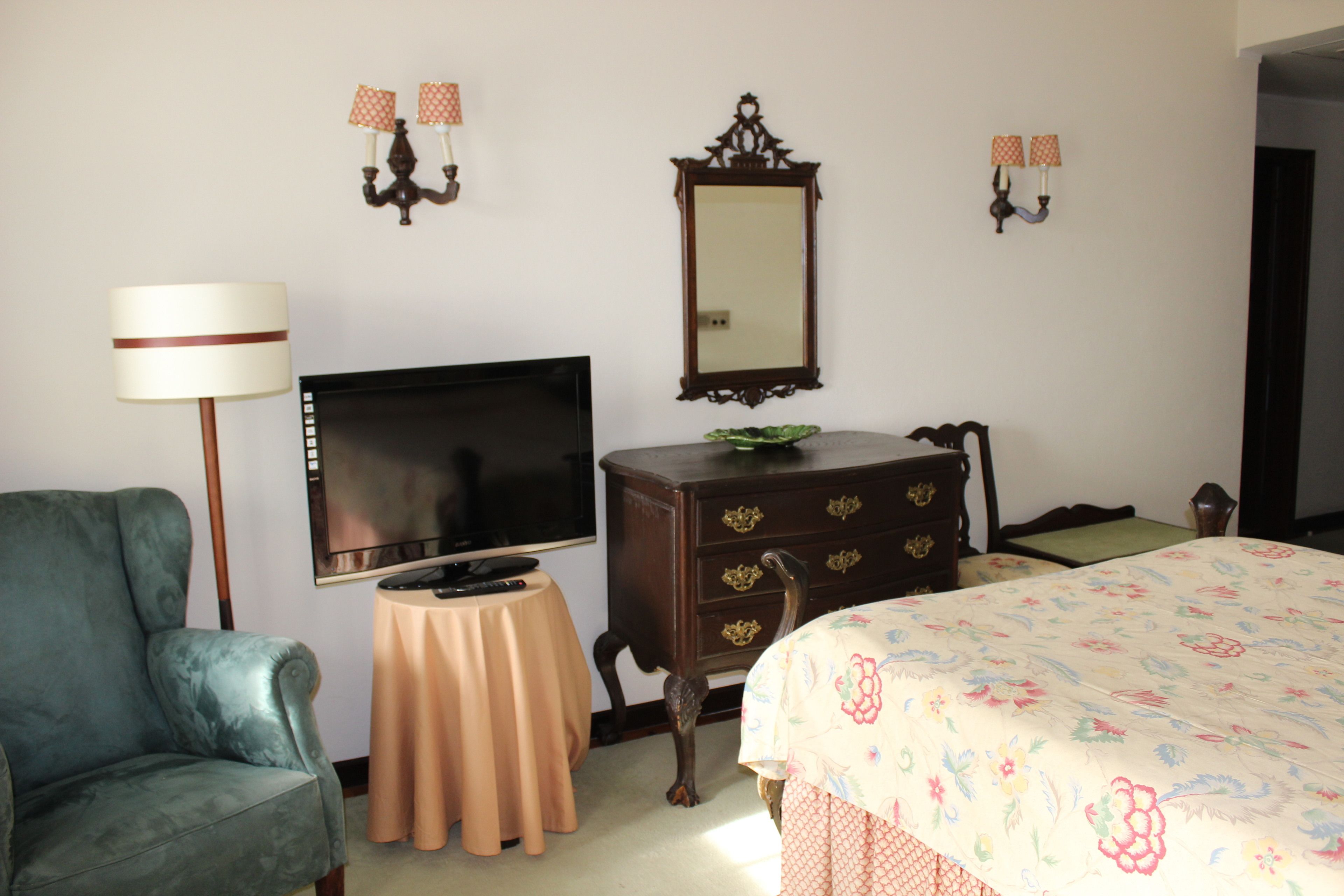 Un dormitorio con cama, televisor, cómoda, silla y una mesita.