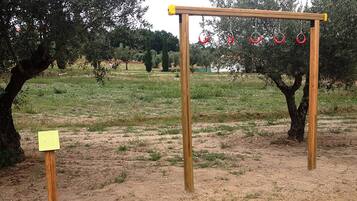 Una struttura in legno all'aperto con anelli appesi, immersa in un prato con alberi sullo sfondo.