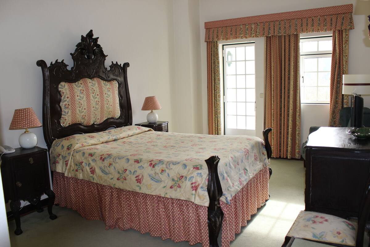 Un dormitorio con una cama grande, una mesita de noche, una silla y un aparador.