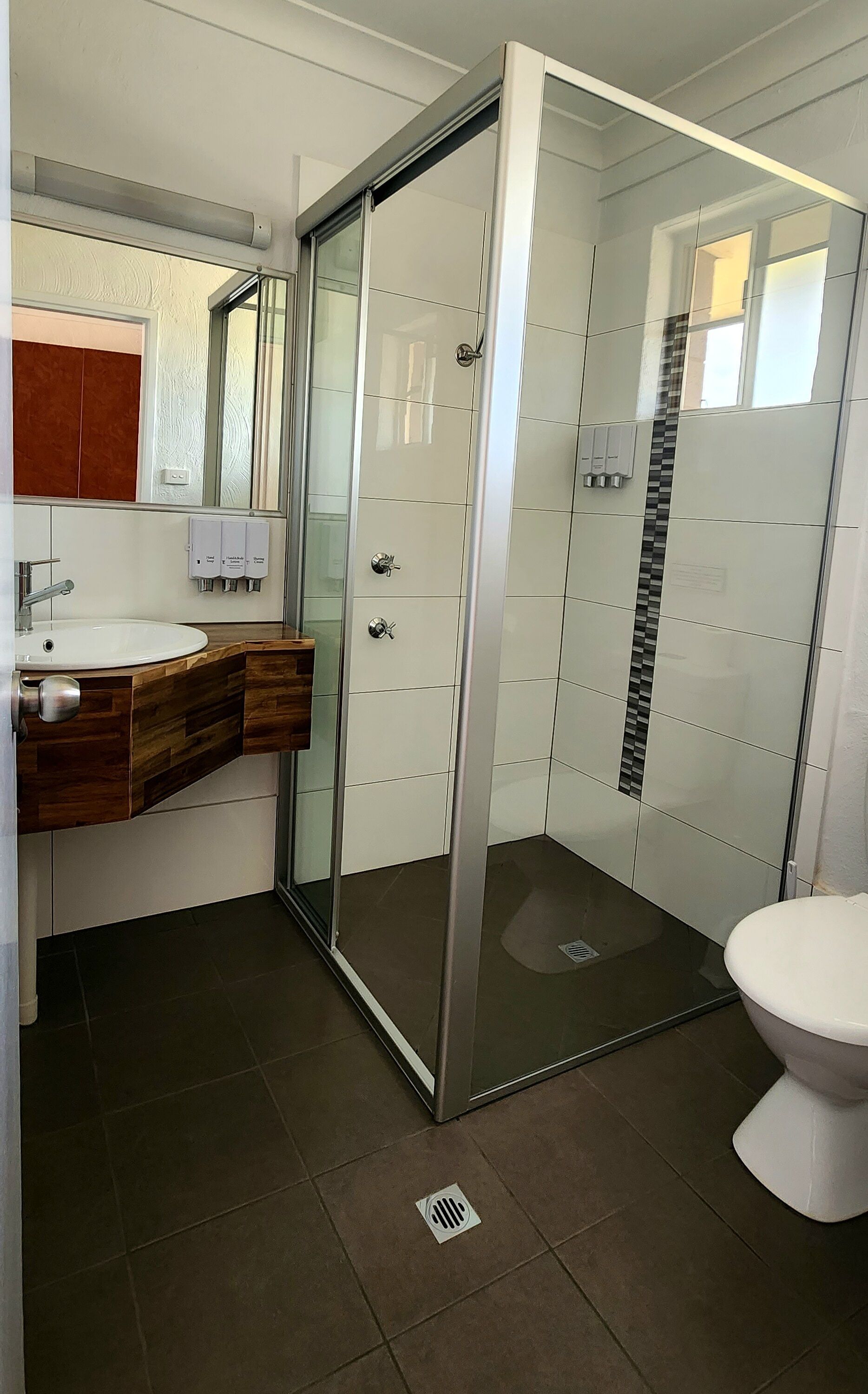A modern bathroom with a glass shower enclosure, a wooden vanity, a white sink, and a toilet.